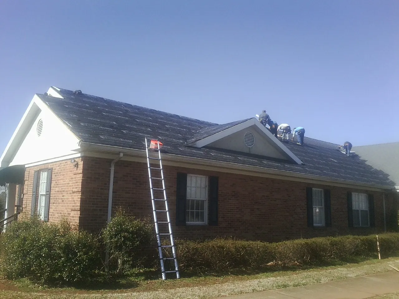Crew tearing shingles off a brick ranch roof with a ladder set — Emergency Roof Repair work by our crew in Culloden