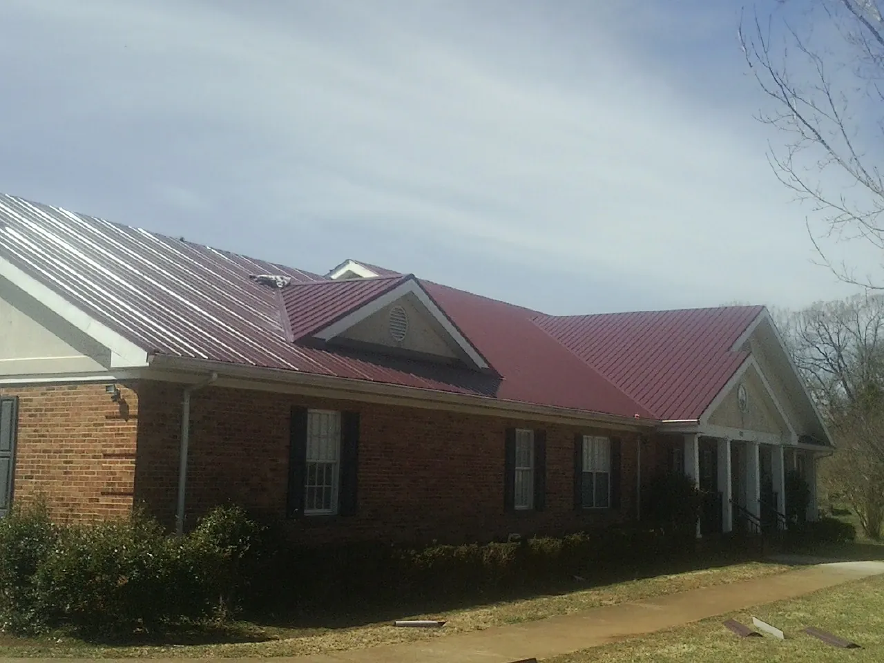 Red metal roof with gabled entries on a long brick building, from a Hail Damage Roof Repair job in Culloden