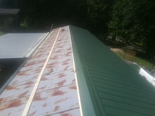 Old rusted panels beside newly installed green metal roofing — Wind Damage Roof Repair by Roofing Brothers in Culloden