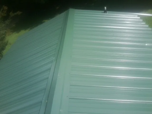 New green metal panels meeting at the ridge of a roof — Flat Roof Repair work by our crew in Culloden