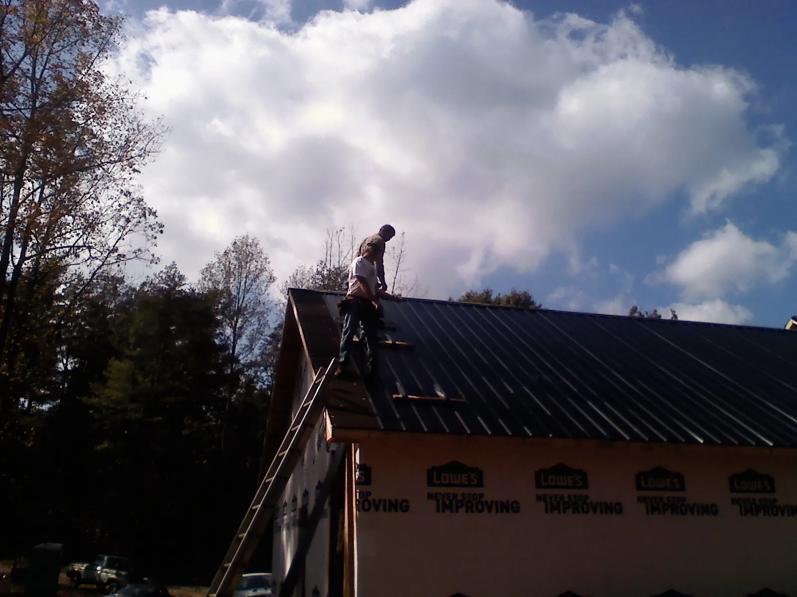 Roofer fastening dark metal panels high against a cloudy sky, from a Roof Inspection job in Culloden