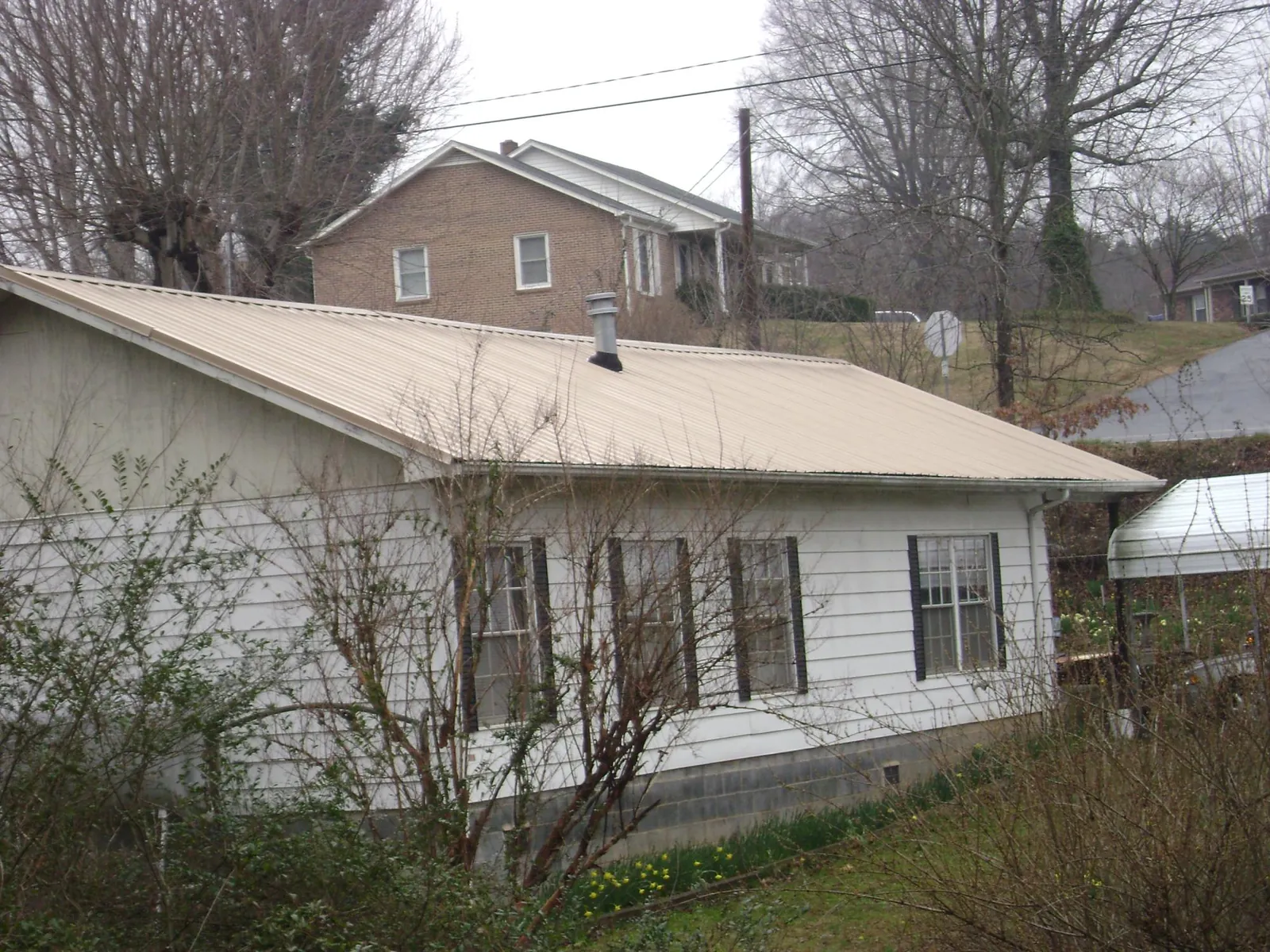 Tan metal roof on a white sided house set into a hillside — Commercial Roofing by Roofing Brothers in Culloden
